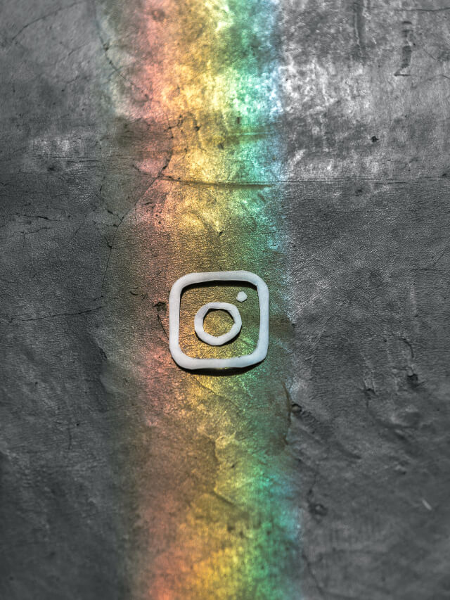 Instagram logo with a rainbow in the background on a textured grey surface