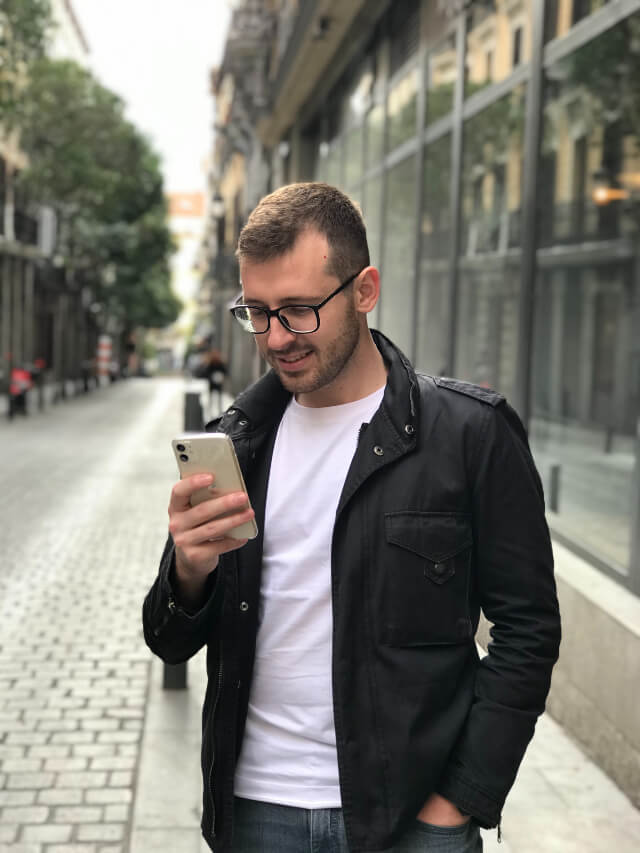 A man standing on the street, busy using his mobile device.